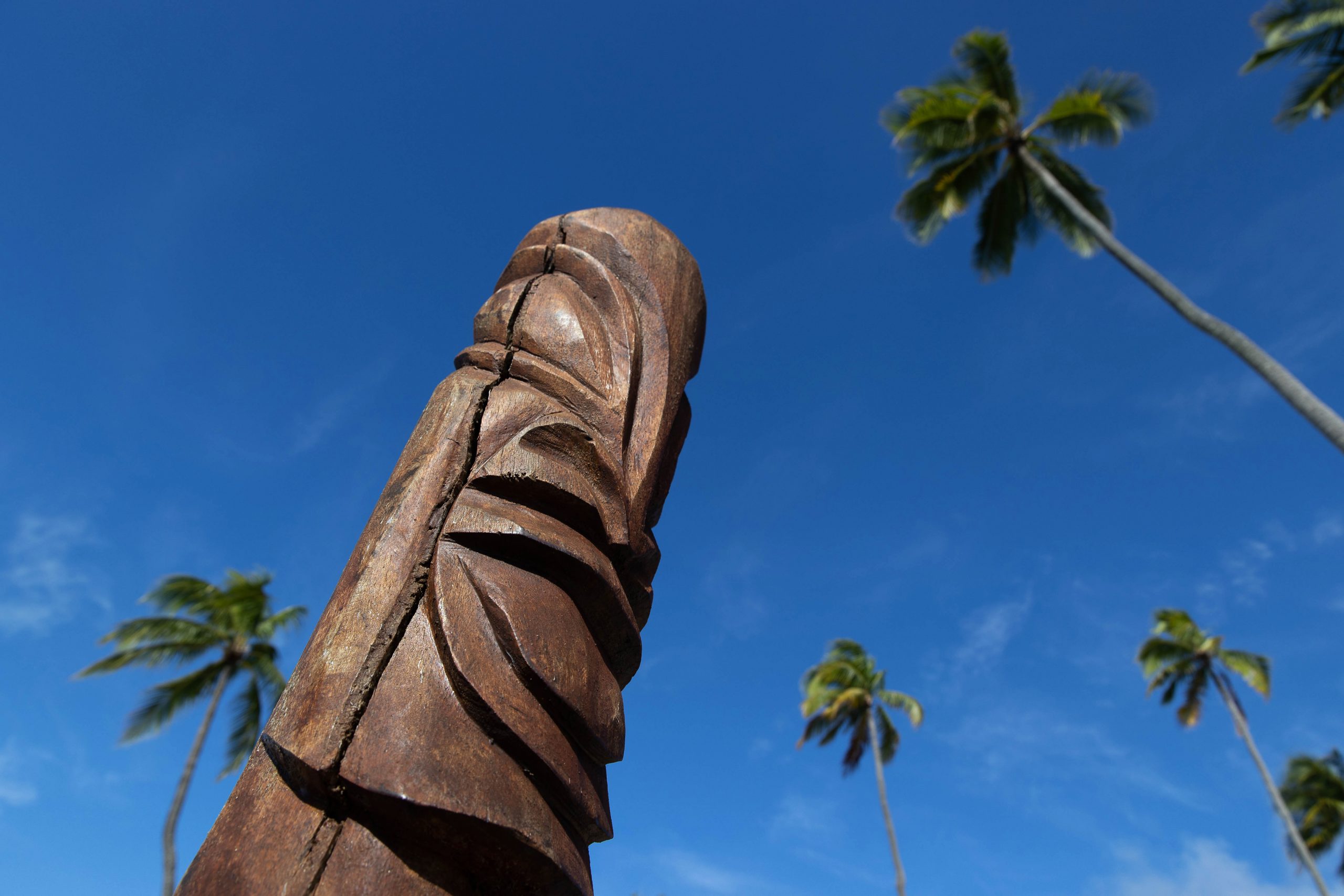 Wood carved tiki under a blue sky and palm trees on the island of Moorea